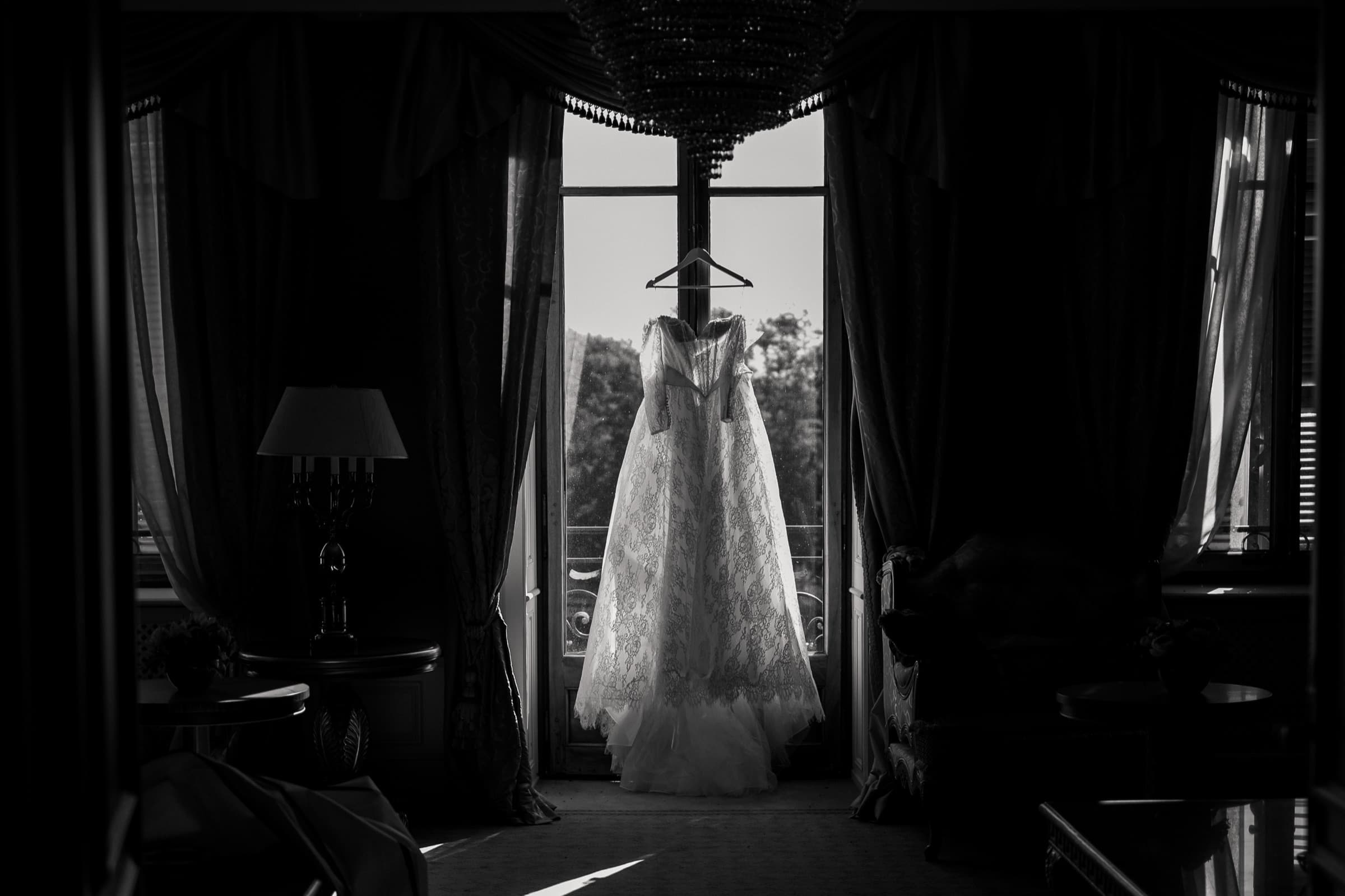 La robe de dentelle suspendue à contre-jour devant une porte-fenêtre, sous un lustre de cristal, en noir et blanc — Château de Crassy