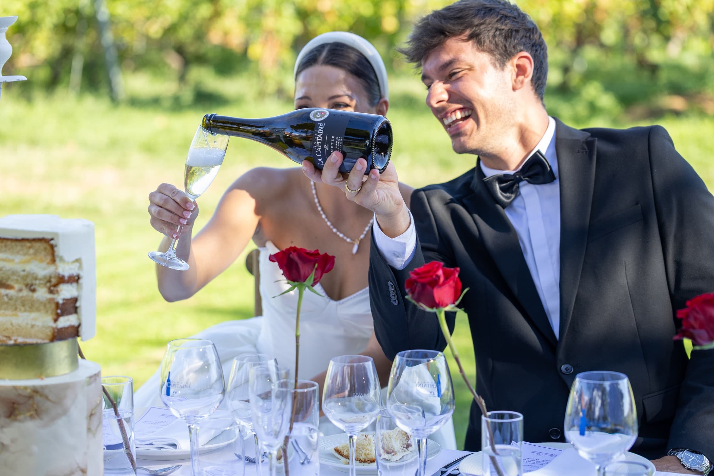 Le marié verse la cuvée du Domaine La Capitaine dans la coupe de la mariée, table dressée dans les vignes — la Côte vaudoise