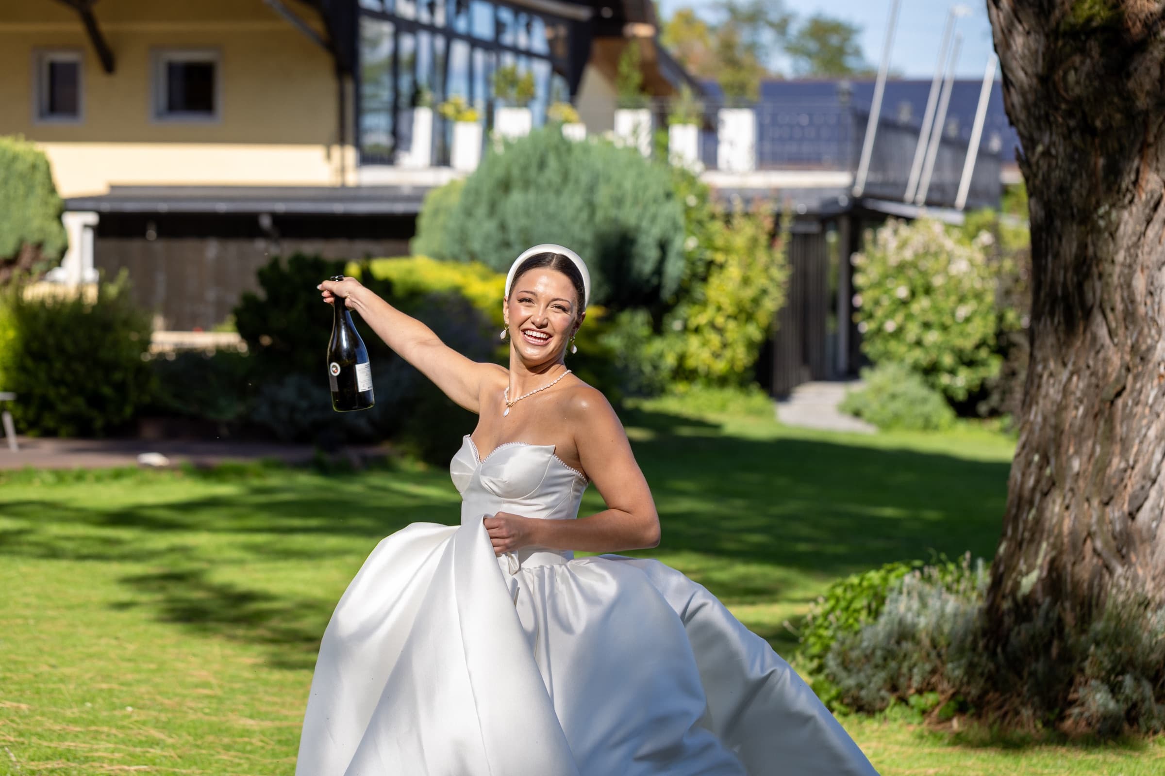 La mariée brandit une bouteille du domaine en riant sur la pelouse — éditorial mariage Domaine La Capitaine, Gland