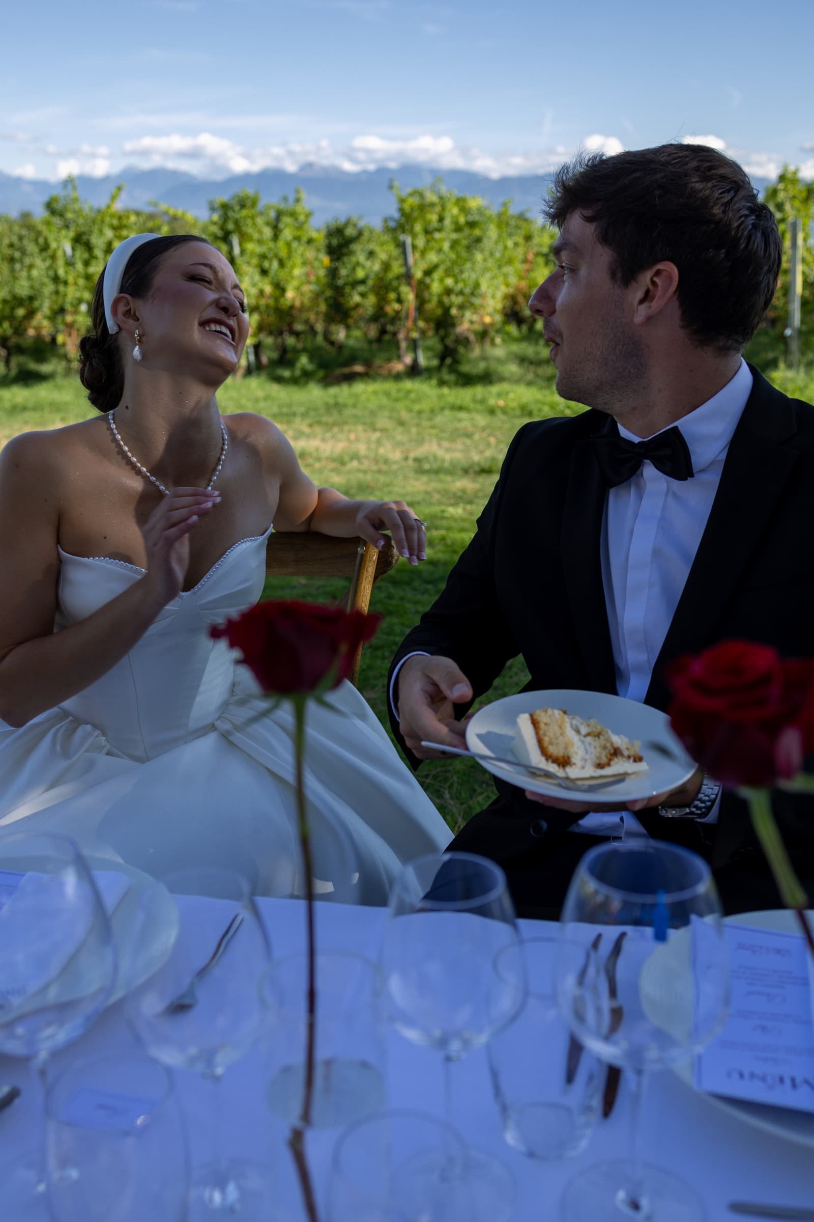 Rires à table entre les rangs de vigne, part de gâteau et roses rouges, Alpes en toile de fond — éditorial mariage Domaine La Capitaine