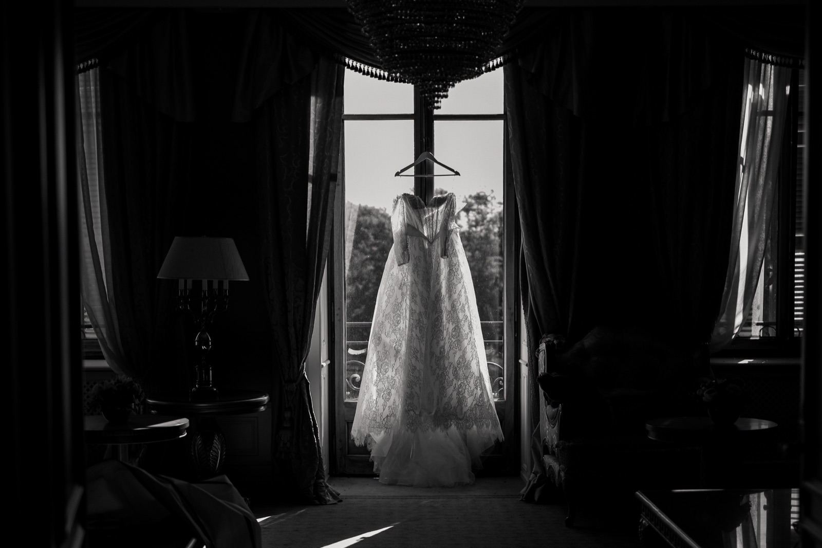 Photographe mariage luxe Genève — Robe mariee dentelle suspendue fenetre noir blanc — Benjamin Pierre